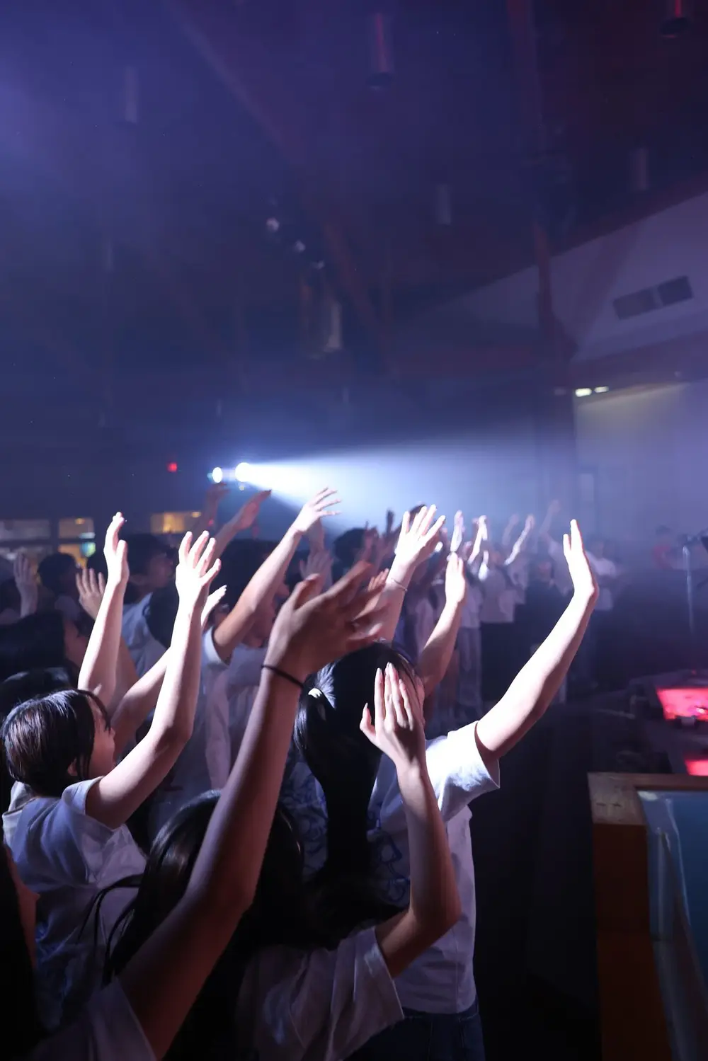 Students with hands raised in worship under stage lights at a Ruwa Worship Night