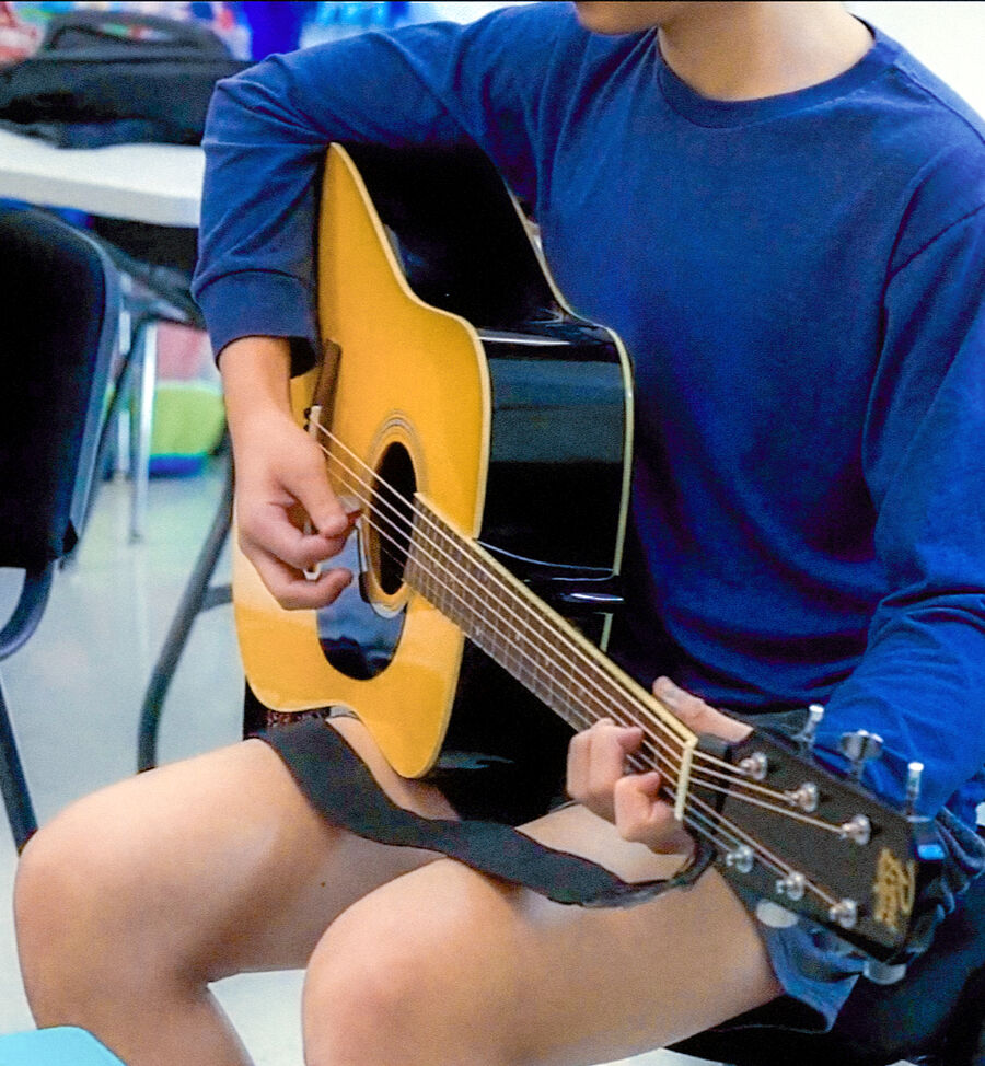 Student playing an acoustic guitar in class