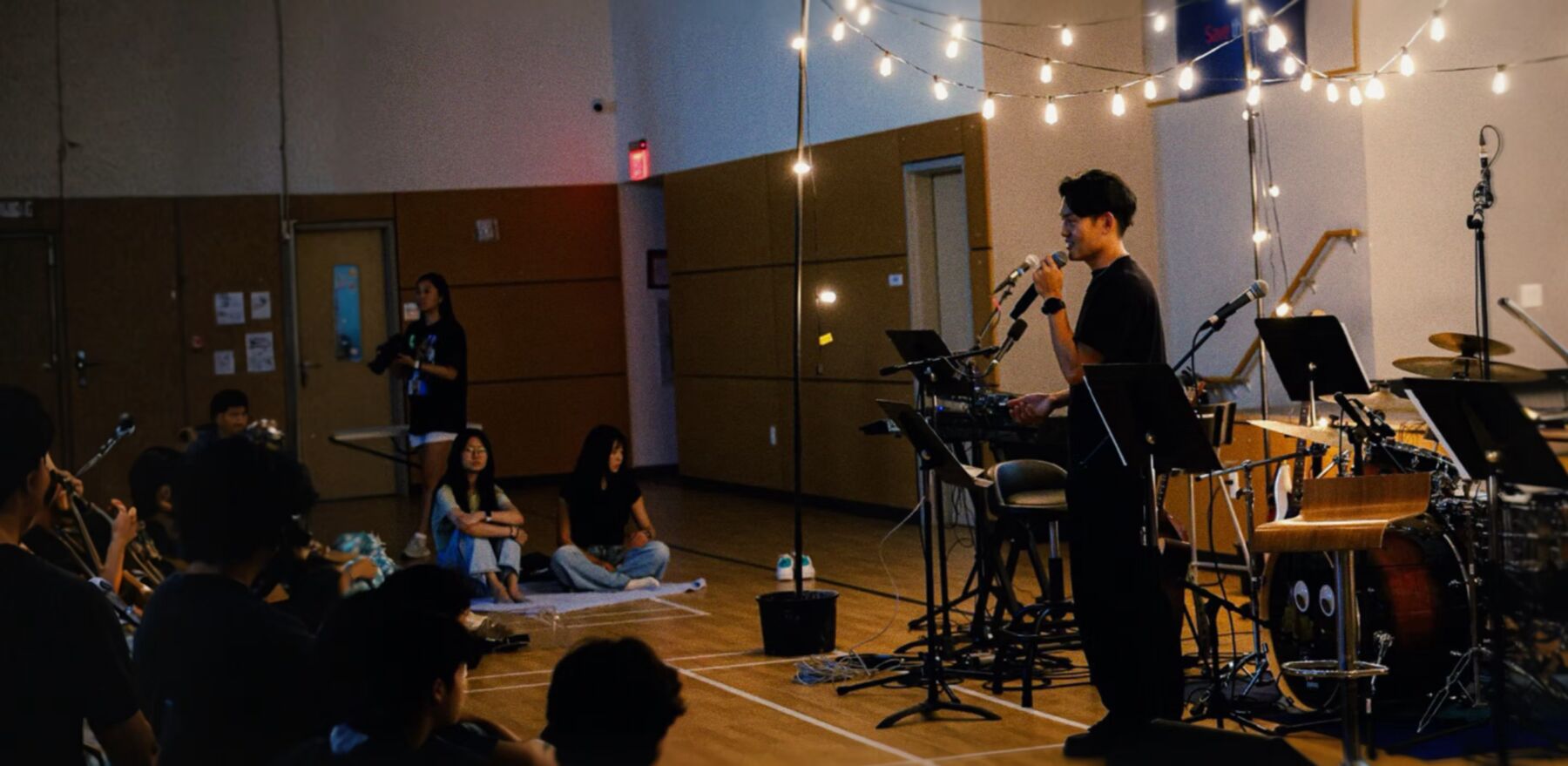Instructor speaking to students under string lights, with the band set up behind him