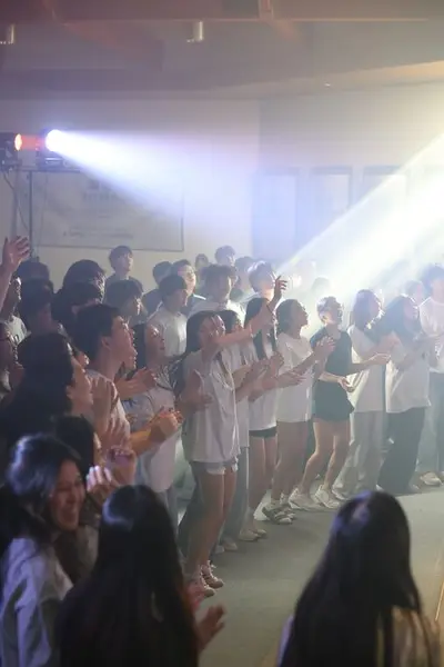 Students singing and clapping under stage lights